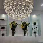 Welcoming reception area with chandelier and display shelves with flowers at Joyful Massage & Spa